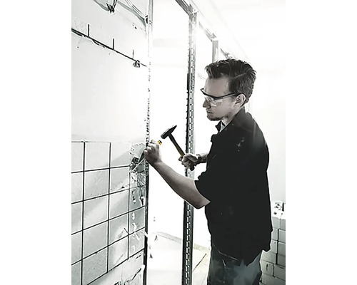 Ein Mann schlägt mit einem Hammer und einem Meißel Fliesen von einer Wand ab.