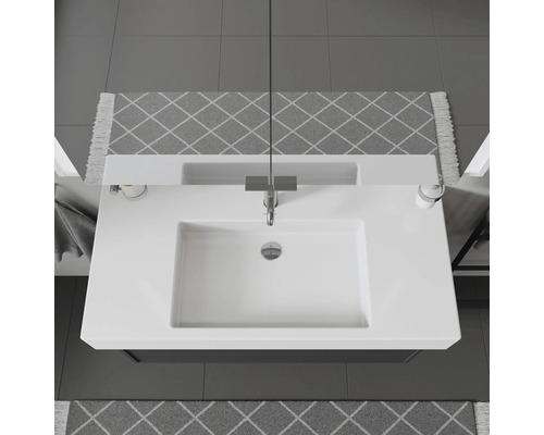 Draufsicht auf ein Waschbecken mit Armatur, Seifenspender und gemusterten Teppichen im Badezimmer.