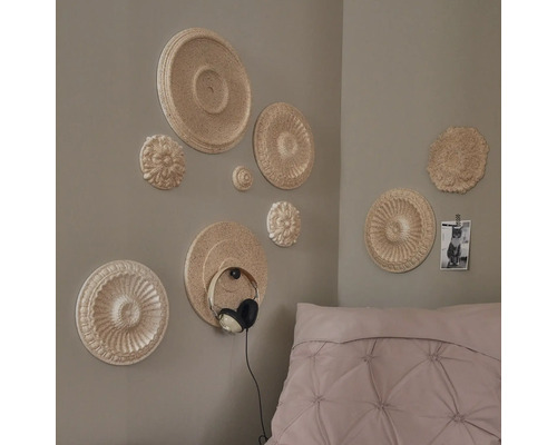 Wanddekoration mit Stuckrosetten in einem Schlafzimmer mit Bett und Foto an der Wand.