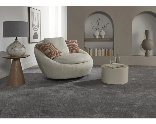 Innenaufnahme eines Wohnzimmers mit grauer Auslegware, einem Sessel, einem Tisch und dekorativen Elementen