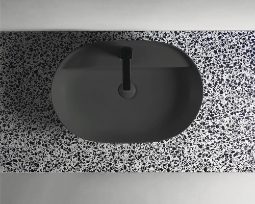Aufsicht auf ein ovales, schwarzes Aufsatzwaschbecken mit Armatur auf einer Arbeitsplatte mit Terrazzo-Muster.