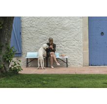 Frau mit Hund auf Gartenbank vor Hauswand