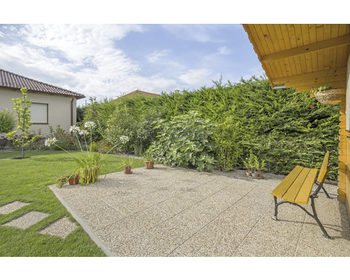 Terrasse mit Kiesbelag und Gartenmöbeln vor grüner Hecke