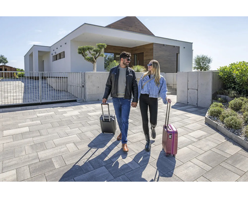 Ein Paar mit Gepäck auf einem gepflasterten Weg zu einem modernen Haus.