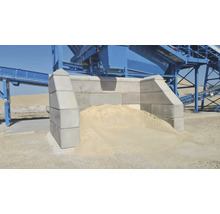 Graue Betonmauern mit Sandhaufen und Förderanlage im Hintergrund