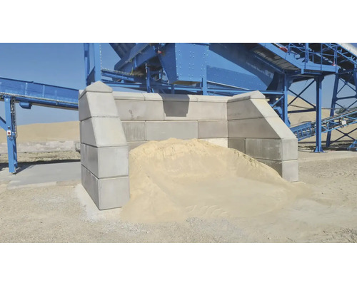 Graue Betonmauern mit Sandhaufen und Förderanlage im Hintergrund