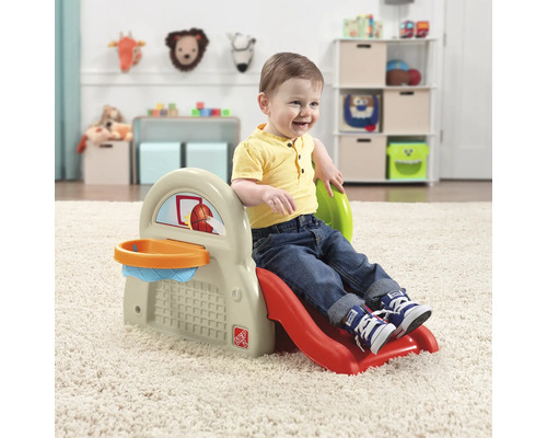 Kleinkind spielt auf einer Kinderrutsche mit Basketballkorb im Innenbereich.