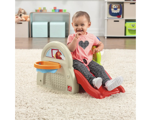 Ein Kind sitzt auf einer Step2 Kinderrutsche mit Basketballkorb in einem Spielzimmer.