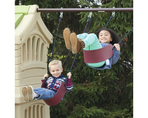 Zwei Kinder schwingen auf einer Kinderschaukel vor einem Spielturm.