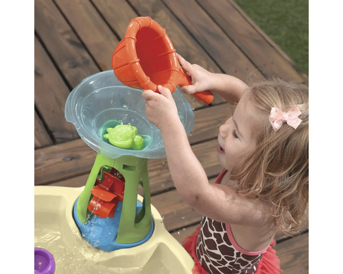 Mädchen spielt mit einem Wasserspieltisch im Freien mit Trichter, Wasserrad und Schildkröte