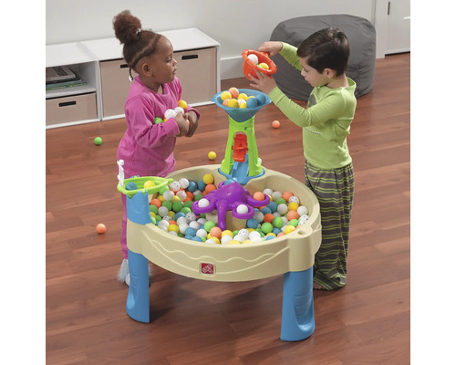 Zwei Kinder spielen mit einem Spieltisch und bunten Bällen.