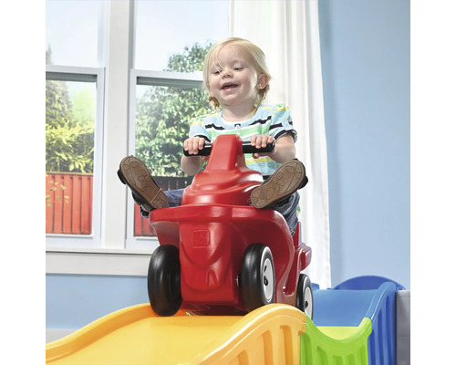 Kind fährt mit einem roten Spielzeugauto eine Spielzeugachterbahn hinunter