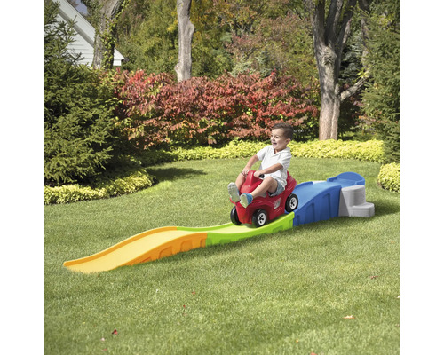 Kind auf rotem Spielzeugauto mit Bahn im Garten