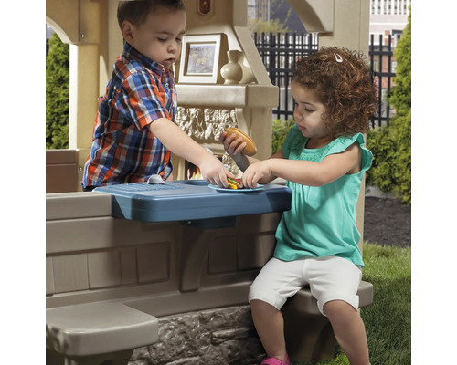 Zwei Kinder spielen mit einem Outdoor-Spielhaus mit Spielküche.