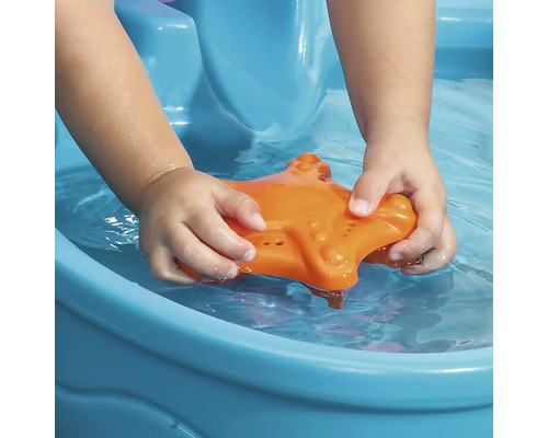 Kind spielt mit einem orangefarbenen Seestern in einem blauen Planschbecken.