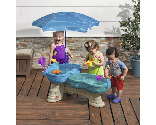 Kinder spielen an einem Wasser-Spieltisch mit Sonnenschirm im Freien.