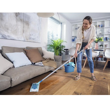 Frau wischt Holzboden mit einem Mopp in einem Wohnzimmer