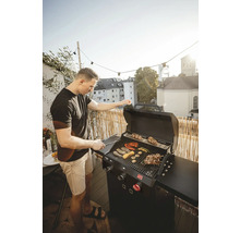 Mann grillt Gemüse und Fleisch auf einem Gasgrill auf einem Balkon
