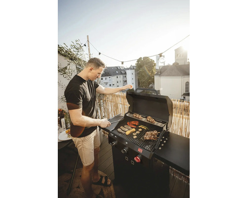 Mann grillt Gemüse und Fleisch auf einem Gasgrill auf einem Balkon