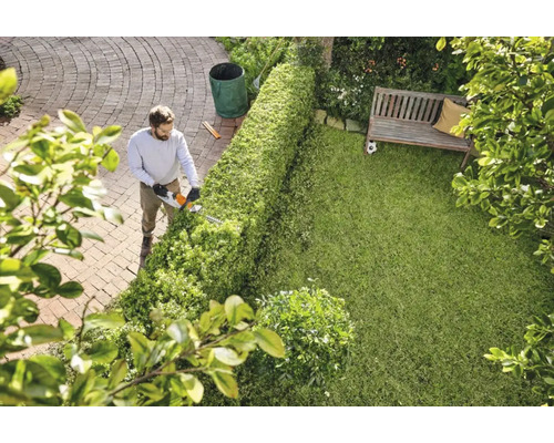 Mann schneidet Hecke mit Heckenschere im Garten.