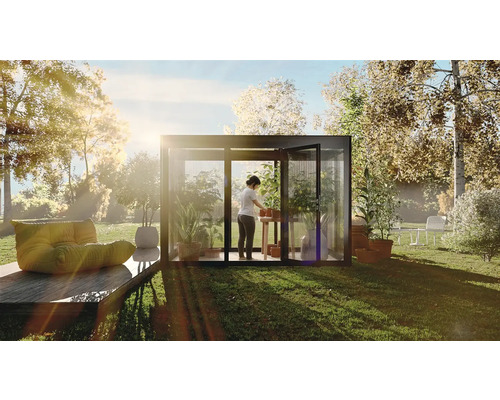 Ein Gewächshaus im Garten mit einer Person, die Pflanzen auf einem Tisch umtopft, umgeben von Grünflächen und Bäumen.