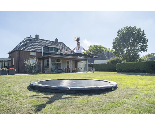 Eine Frau springt auf einem runden Gartentrampolin vor einem Haus.
