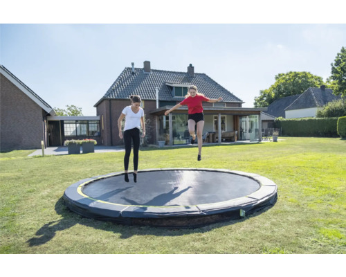 Zwei Frauen springen auf einem runden Gartentrampolin auf einer Wiese.