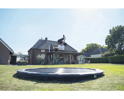 Eine Person macht einen Salto auf einem Trampolin im Garten.