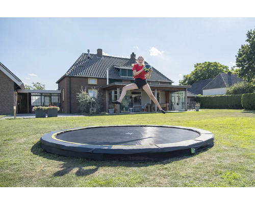 Mädchen springt mit Ball auf Gartentrampolin vor Haus