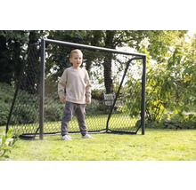 Ein Junge steht vor einem Fußballtor im Garten.