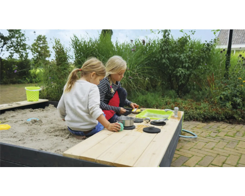 Zwei Kinder spielen an einem Sandkasten mit Spielküche im Garten.