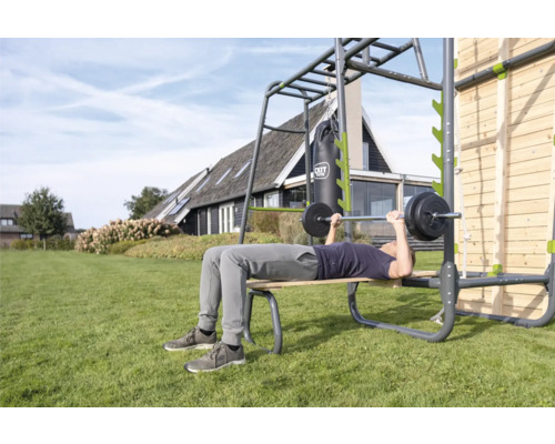 Mann beim Bankdrücken auf einer Outdoor-Fitnessanlage im Garten