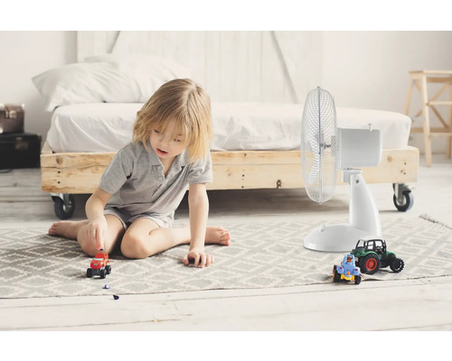 Helles Zimmer mit einem Jungen, der auf einem Teppich neben einem Ventilator und Spielzeugautos sitzt
