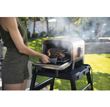 Eine Frau nimmt einen Braten aus einem Grill im Freien.