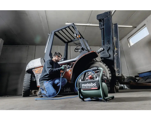 Mann arbeitet mit einem Metabo Kompressor an einem Gabelstapler in einer Werkstatt.