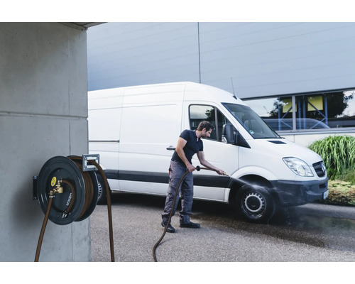 Mann reinigt Transporter mit einer Schlauchtrommel an einer Betonwand montiert