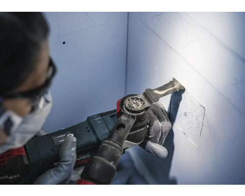 Eine Person benutzt ein Multifunktionswerkzeug, um eine Aussparung in einer Wand zu schneiden.