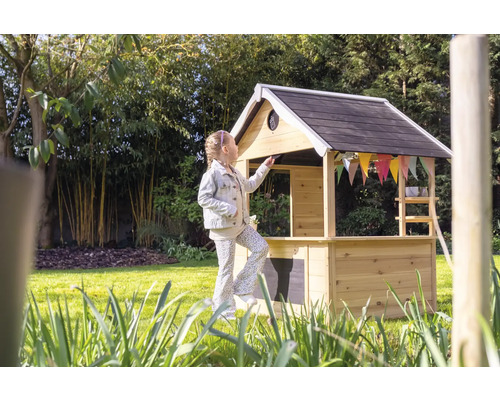 Mädchen vor Spielhaus aus Holz im Garten.