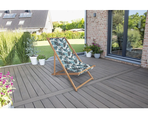 Gartenszene mit einem Liegestuhl mit Blattmuster auf einer Terrasse.