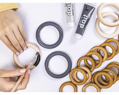 "Eine Person bemalt einen Holzring mit einem Pinsel