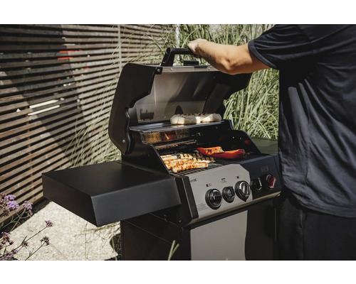 Gasgrill mit Speisen auf dem Rost und einer Person, die den Deckel öffnet