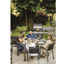 Szene im Freien mit einem Gasgrill, einem Esstisch und vier Personen beim Essen.