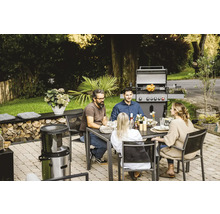 Personen sitzen an einem Gartentisch mit Grill im Hintergrund.