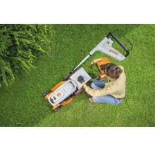 Aufsicht einer Frau, die einen Rasenmäher auf einer Rasenfläche vorbereitet. Stihl Logo.