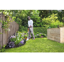 Gärtner schneidet Rasenkanten mit einem Kantenschneider in einem Garten mit Holzzaun und Hochbeet