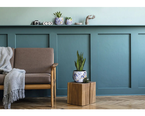 Wohnzimmer mit Sofa, Pflanzentisch und Wandregal für Dekorationen.