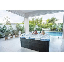 Paar entspannt in einem sprudelnden Whirlpool im Freien, neben einem Pool und Garten.