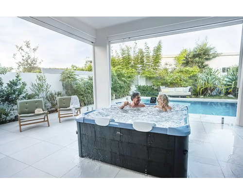 Paar entspannt in einem sprudelnden Whirlpool im Freien, neben einem Pool und Garten.