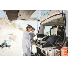Zwei Personen kochen auf einem Auszug-Kochfeld am Heck eines Fahrzeugs am Strand.