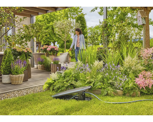 Garten mit Regner und einer Frau, die Pflanzen bewässert